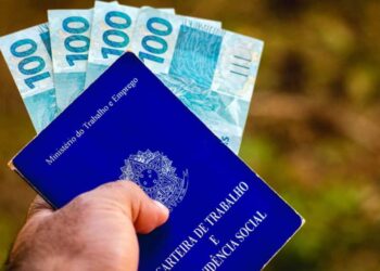 July 28, 2021, Brazil. In this photo illustration the a man displays his Work and Social Security Card in Brazil with three hundred reais bills