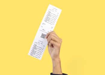 close up de mão segurando nota fiscal em frente ao um fundo amarelo