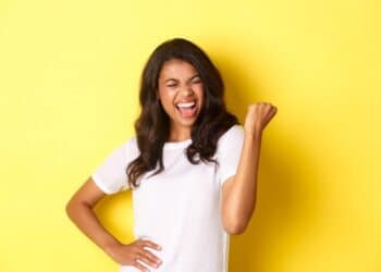 mulher negra feliz fotografada em frente a parede amarela