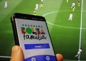 pessoa segurando smartphone com imagem de jogo esportivo ao fundo