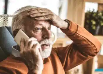 idoso falando ao celular com a mão na testa com semblante de surpreso negativamente