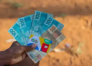 close up mão segurando notas de 100, 50 e cartão do bolsa família