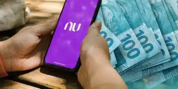 close up mão segurando smartphone com app do nubank aberta e ao fundo notas de 100