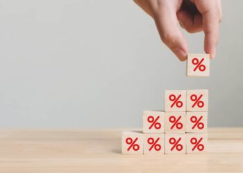 Imagem mostra uma mão colocando um bloco com símbolo de porcentagem em cima de outros blocos, simbolizando crescimento e aumento de valores.