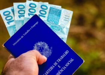 July 28, 2021, Brazil. In this photo illustration the a man displays his Work and Social Security Card in Brazil with three hundred reais bills