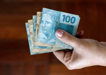 mão segurando notas de dinheiro de cem e cinquenta reais