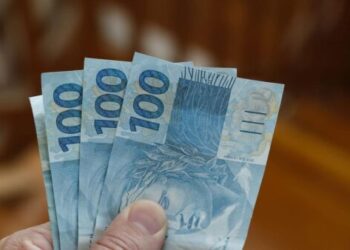 mão segurando notas de cem reais